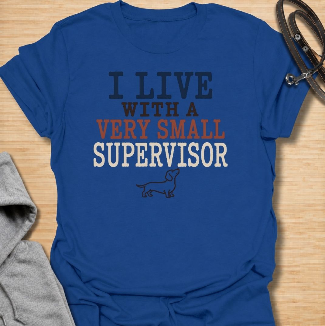 A funny dachshund T-shirt for anyone who lives with a very small dog who insists on overseeing absolutely everything. Featuring the phrase “I Live With a Very Small Supervisor” and a simple dachshund illustration, this design captures the breed’s curious, watchful personality perfectly. Ideal for dachshund moms, dachshund dads, sausage dog owners, and anyone whose little dog follows them from room to room. A playful everyday tee for fans of dachshund humor, wiener dogs, and devoted four-legged supervisors.