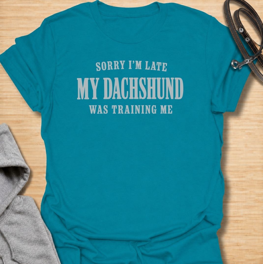 A funny dachshund T-shirt for anyone who knows the dog is usually the one in charge. Featuring the phrase “Sorry I’m Late, My Dachshund Was Training Me,” this clean text-based design plays on the breed’s stubborn, clever personality. Perfect for dachshund moms, dachshund dads, sausage dog owners, and anyone whose plans regularly revolve around their dog. A simple everyday tee for fans of dachshund humor, funny dog sayings, and breed-specific gifts.