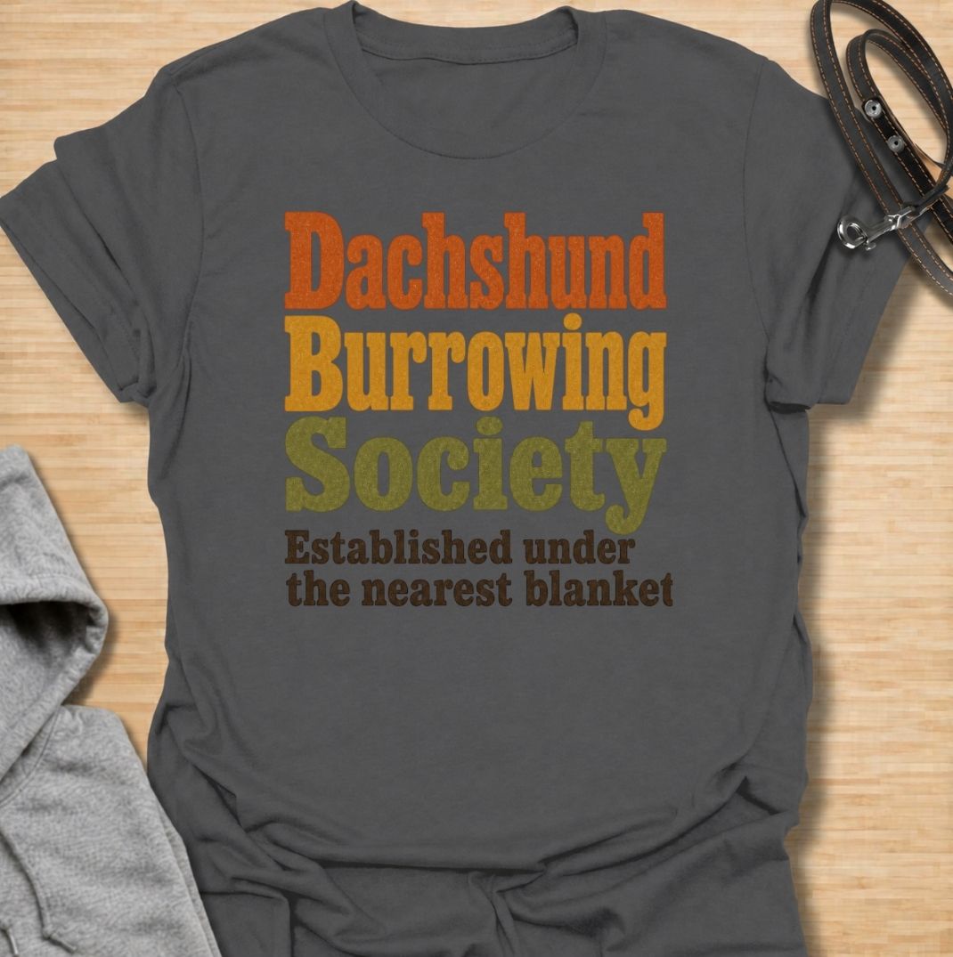 A funny dachshund T-shirt for anyone who knows the fastest way to find a sausage dog is to check under the nearest blanket. Featuring the phrase “Dachshund Burrowing Society — Established Under the Nearest Blanket,” this retro text design celebrates one of the breed’s most familiar habits. Perfect for dachshund moms, dachshund dads, doxie owners, and anyone whose dog treats blankets like a second home. A cozy, humorous everyday tee for fans of dachshund personality, burrowing behavior, and breed-specific do