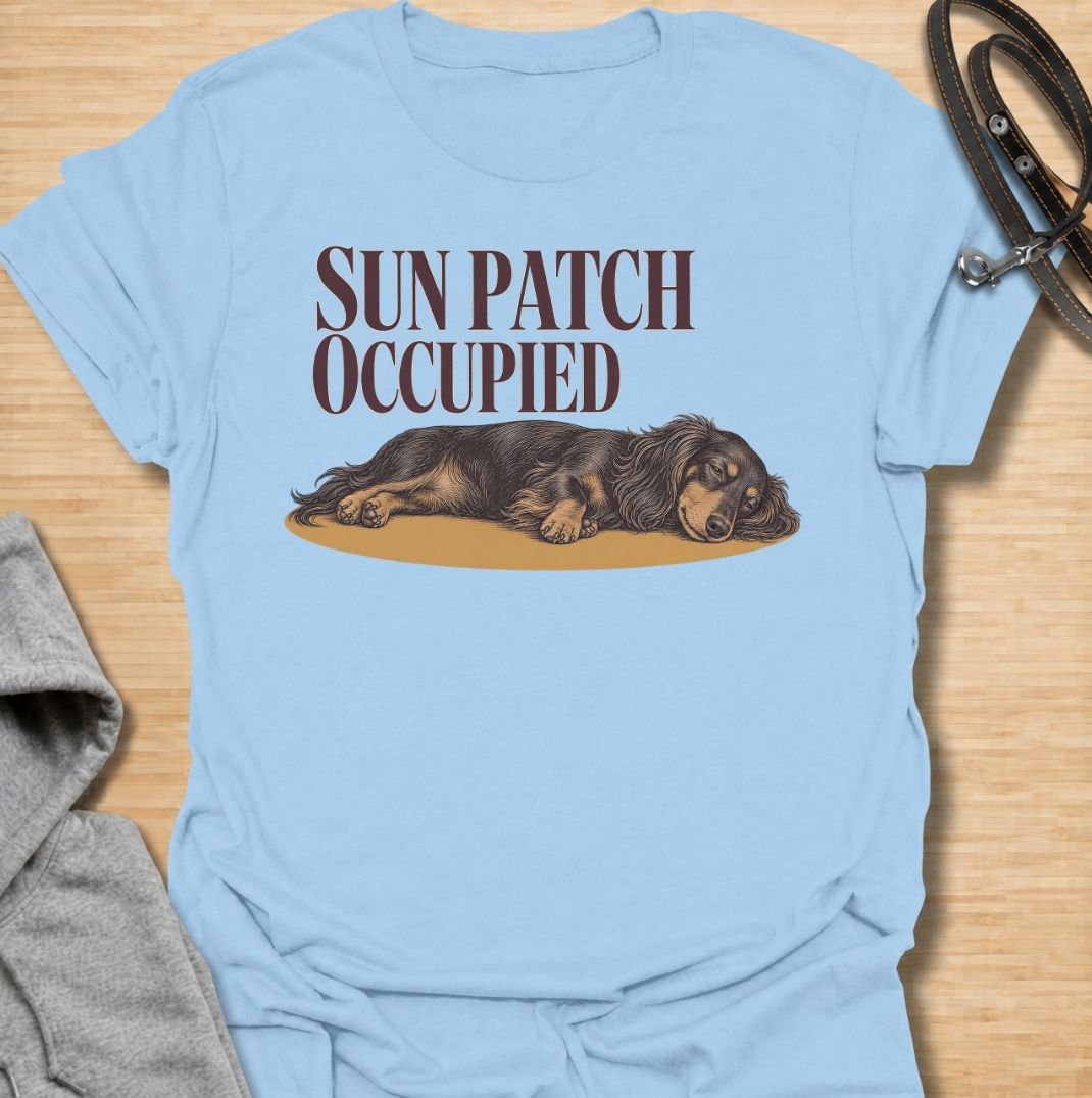 A funny dachshund T-shirt for anyone who knows the best sunny spot in the house is already taken. Featuring the phrase “Sun Patch Occupied” with a relaxed dachshund stretched out in the warmth, this design captures one of the breed’s most familiar little habits. Perfect for dachshund moms, dachshund dads, sausage dog owners, and anyone whose dog follows every patch of sunshine around the room. A cozy everyday tee for fans of dachshund humor, sleepy dogs, and breed-specific gifts.