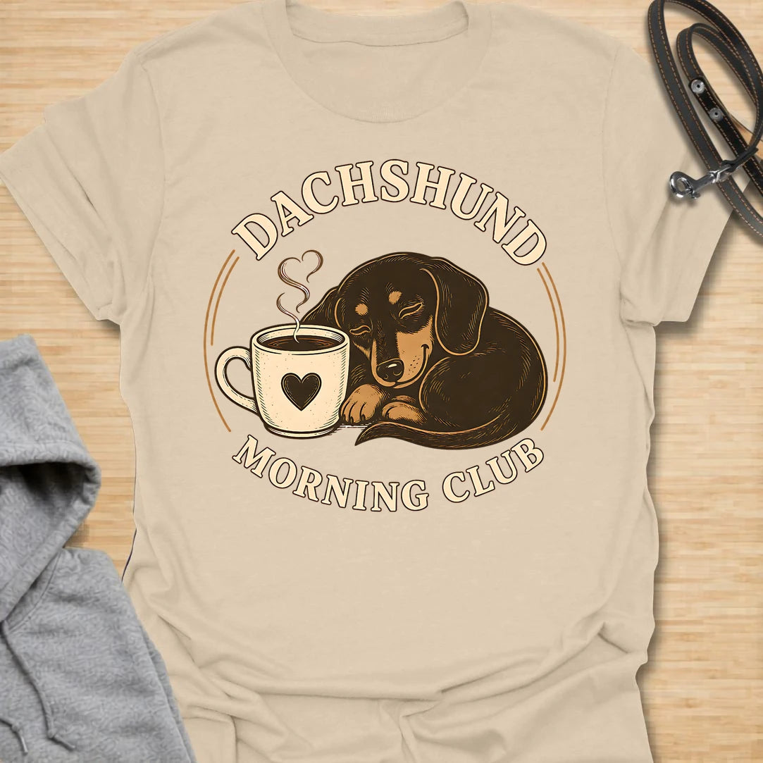 This Dachshund Morning Club t-shirt is made for doxie lovers who know mornings are better with coffee and a little long dog nearby. Featuring a cozy dachshund curled beside a steaming mug with vintage-style circular lettering, this cute dog design is great for dachshund moms, dachshund dads, coffee lovers, wiener dog fans, rescue dog lovers, and anyone whose morning routine includes caffeine and dachshund company.