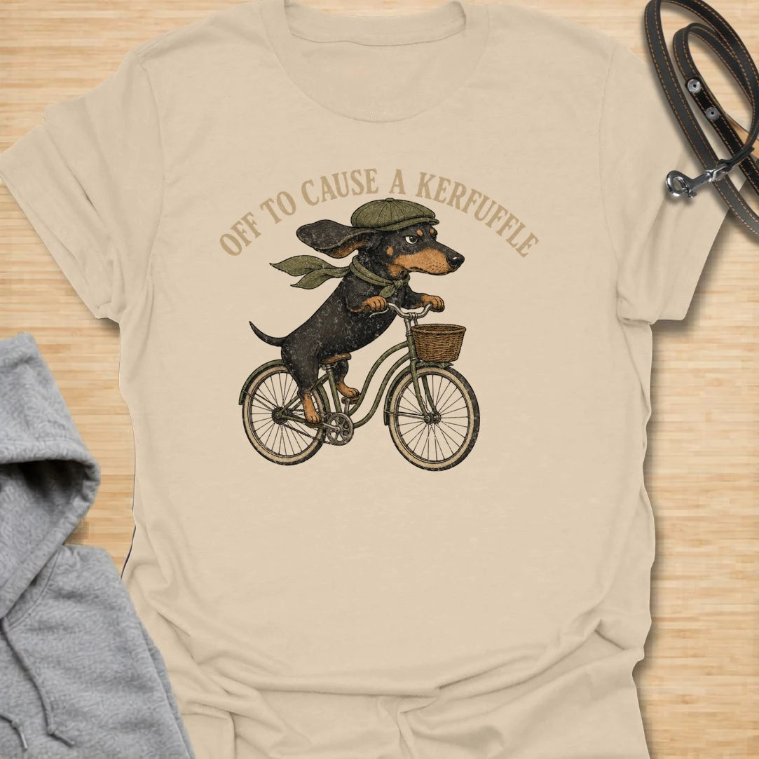 This Off To Cause A Kerfuffle t-shirt is made for dachshund lovers who know their little long dog is always headed somewhere to create a situation. Featuring a determined dachshund riding a vintage bike with flying ears and classic muted colors, this design has a funny chaotic dog-parent feel. Perfect for dachshund moms, dachshund dads, wiener dog fans, rescue dog lovers, and anyone whose doxie is always on a mission.