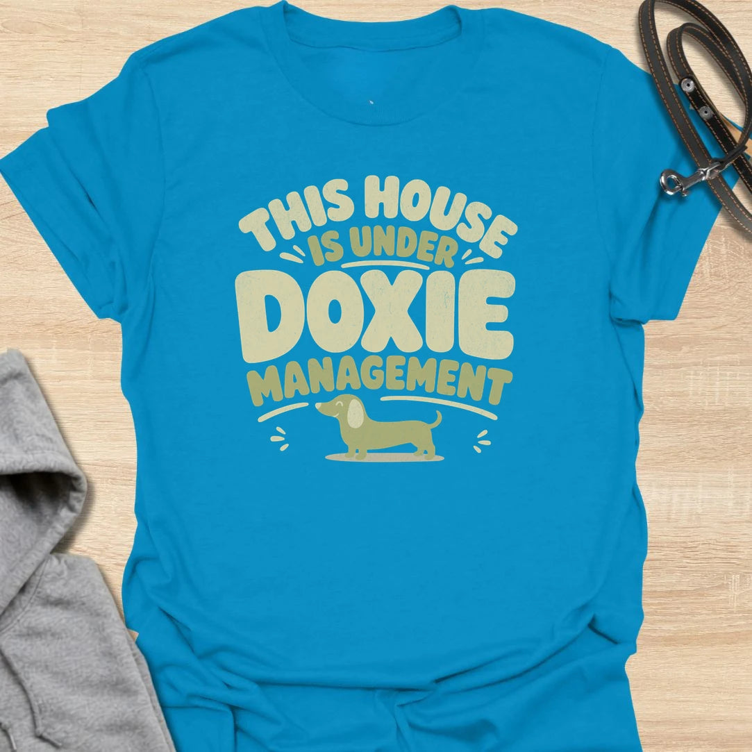 A funny dachshund T-shirt for homes where the smallest resident is clearly in charge. The cheerful retro lettering and little sausage dog perfectly capture life under strict doxie management. A fun gift for dachshund moms, dachshund dads, new puppy owners, and anyone whose dog runs the household.