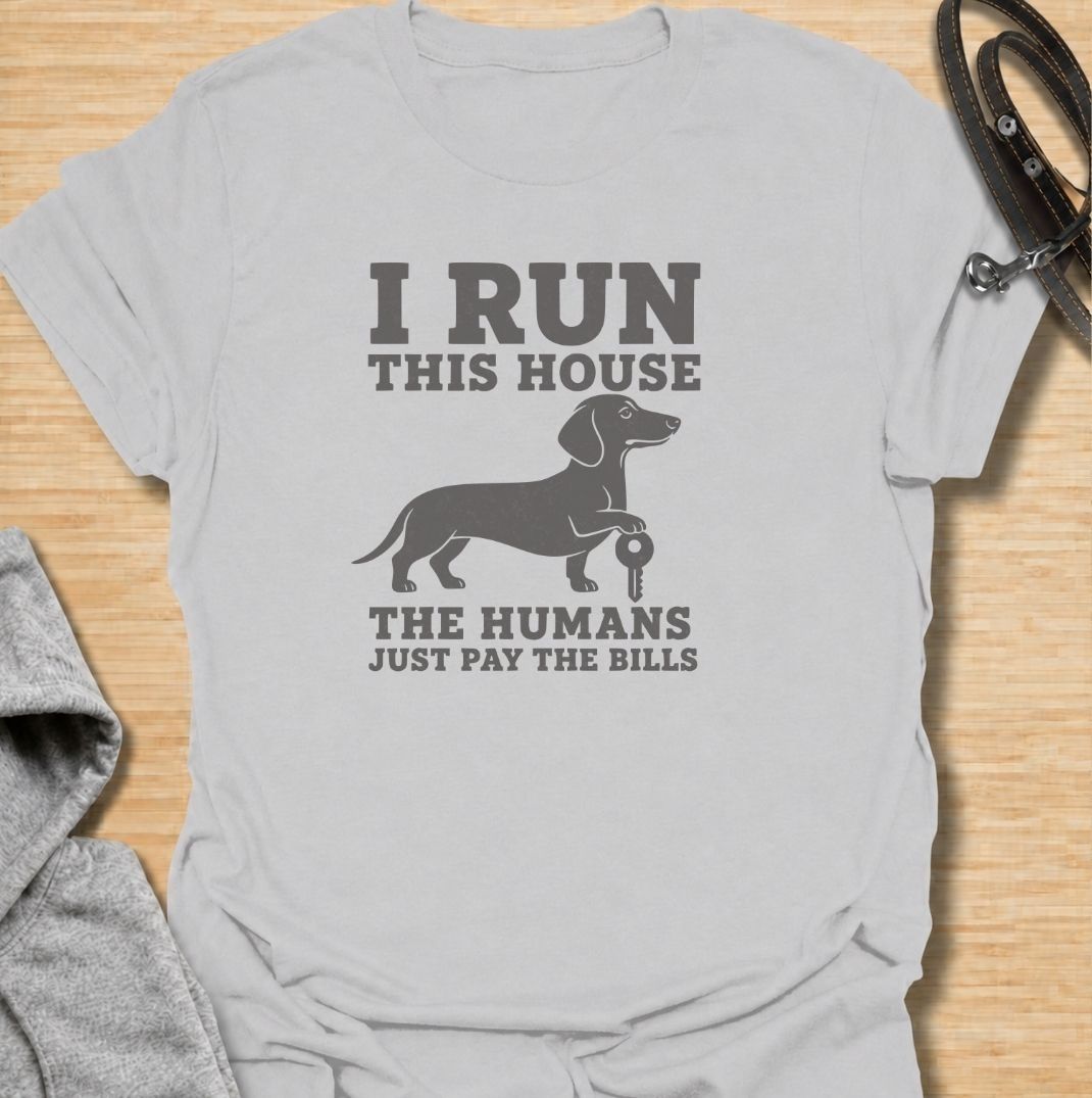 I run this house—the humans just pay the bills. A funny dachshund T-shirt for owners whose confident sausage dog is clearly in charge.