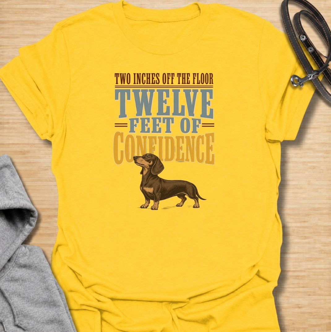For dachshunds who may only be a couple of inches off the floor but carry themselves like they own the entire room. This funny dachshund T-shirt features the phrase “Two Inches Off the Floor, Twelve Feet of Confidence” with a proud little doxie illustration. Perfect for owners who know tiny legs come with enormous personality, attitude and self-belief. A bold vintage-style dog lover tee made for anyone who lives with a fearless sausage dog.
