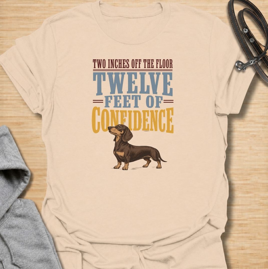 For dachshunds who may only be a couple of inches off the floor but carry themselves like they own the entire room. This funny dachshund T-shirt features the phrase “Two Inches Off the Floor, Twelve Feet of Confidence” with a proud little doxie illustration. Perfect for owners who know tiny legs come with enormous personality, attitude and self-belief. A bold vintage-style dog lover tee made for anyone who lives with a fearless sausage dog.