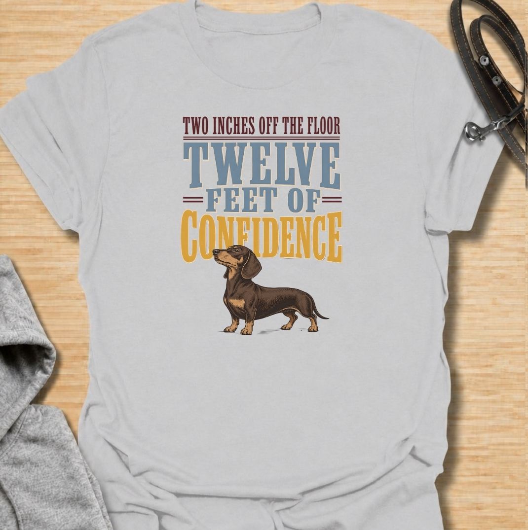 For dachshunds who may only be a couple of inches off the floor but carry themselves like they own the entire room. This funny dachshund T-shirt features the phrase “Two Inches Off the Floor, Twelve Feet of Confidence” with a proud little doxie illustration. Perfect for owners who know tiny legs come with enormous personality, attitude and self-belief. A bold vintage-style dog lover tee made for anyone who lives with a fearless sausage dog.