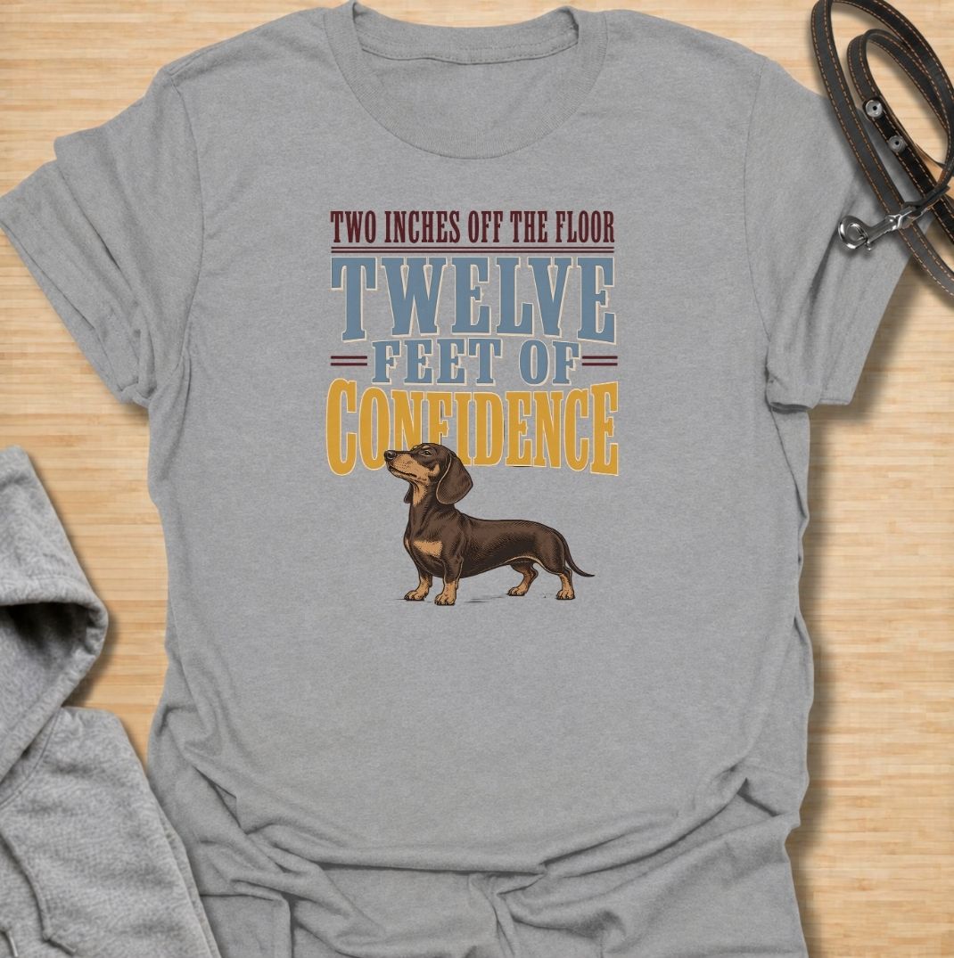 For dachshunds who may only be a couple of inches off the floor but carry themselves like they own the entire room. This funny dachshund T-shirt features the phrase “Two Inches Off the Floor, Twelve Feet of Confidence” with a proud little doxie illustration. Perfect for owners who know tiny legs come with enormous personality, attitude and self-belief. A bold vintage-style dog lover tee made for anyone who lives with a fearless sausage dog.
