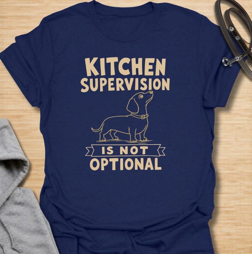 A funny dachshund T-shirt for anyone who never enters the kitchen without their four-legged supervisor close behind. Featuring a clean vintage-inspired dachshund illustration and the phrase “Kitchen Supervision Is Not Optional,” this design captures one of the breed’s most familiar habits. Perfect for dachshund moms, dachshund dads, sausage dog owners, and anyone whose dog appears the moment food is involved. A playful everyday tee for fans of dachshund humor, wiener dogs, and food-obsessed pups.