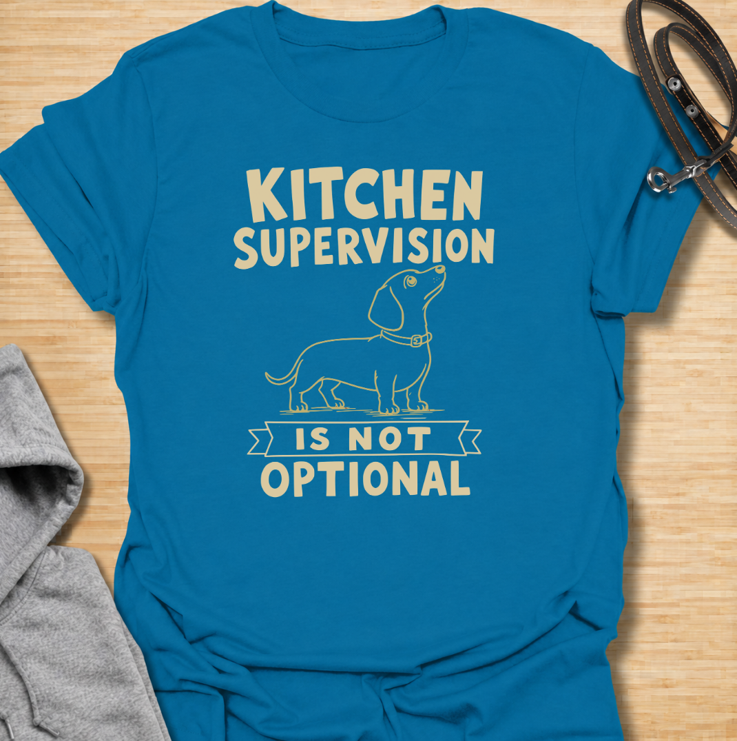 A funny dachshund T-shirt for anyone who never enters the kitchen without their four-legged supervisor close behind. Featuring a clean vintage-inspired dachshund illustration and the phrase “Kitchen Supervision Is Not Optional,” this design captures one of the breed’s most familiar habits. Perfect for dachshund moms, dachshund dads, sausage dog owners, and anyone whose dog appears the moment food is involved. A playful everyday tee for fans of dachshund humor, wiener dogs, and food-obsessed pups.