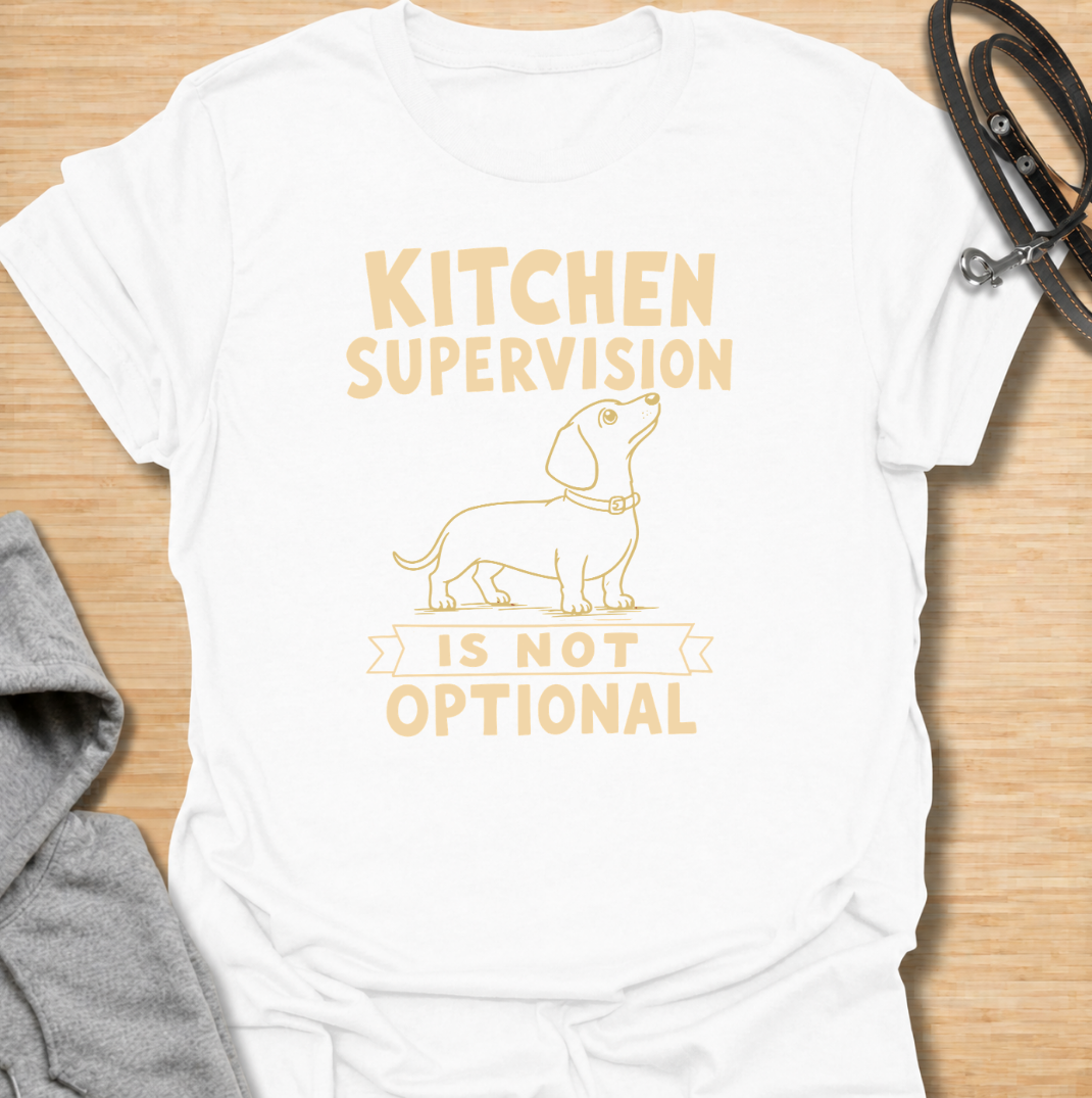 A funny dachshund T-shirt for anyone who never enters the kitchen without their four-legged supervisor close behind. Featuring a clean vintage-inspired dachshund illustration and the phrase “Kitchen Supervision Is Not Optional,” this design captures one of the breed’s most familiar habits. Perfect for dachshund moms, dachshund dads, sausage dog owners, and anyone whose dog appears the moment food is involved. A playful everyday tee for fans of dachshund humor, wiener dogs, and food-obsessed pups.