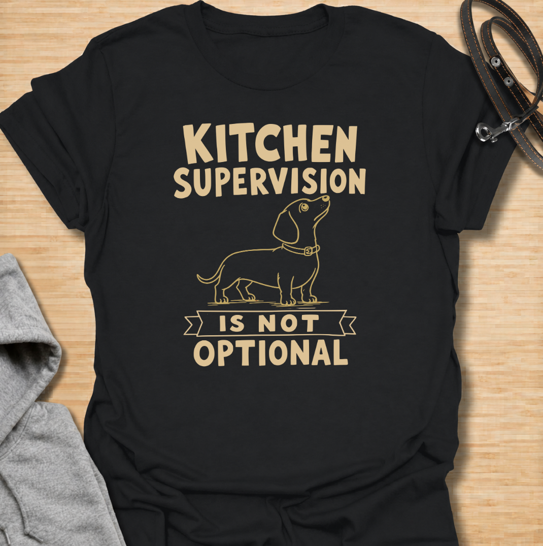 A funny dachshund T-shirt for anyone who never enters the kitchen without their four-legged supervisor close behind. Featuring a clean vintage-inspired dachshund illustration and the phrase “Kitchen Supervision Is Not Optional,” this design captures one of the breed’s most familiar habits. Perfect for dachshund moms, dachshund dads, sausage dog owners, and anyone whose dog appears the moment food is involved. A playful everyday tee for fans of dachshund humor, wiener dogs, and food-obsessed pups.