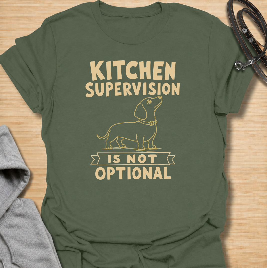 A funny dachshund T-shirt for anyone who never enters the kitchen without their four-legged supervisor close behind. Featuring a clean vintage-inspired dachshund illustration and the phrase “Kitchen Supervision Is Not Optional,” this design captures one of the breed’s most familiar habits. Perfect for dachshund moms, dachshund dads, sausage dog owners, and anyone whose dog appears the moment food is involved. A playful everyday tee for fans of dachshund humor, wiener dogs, and food-obsessed pups.