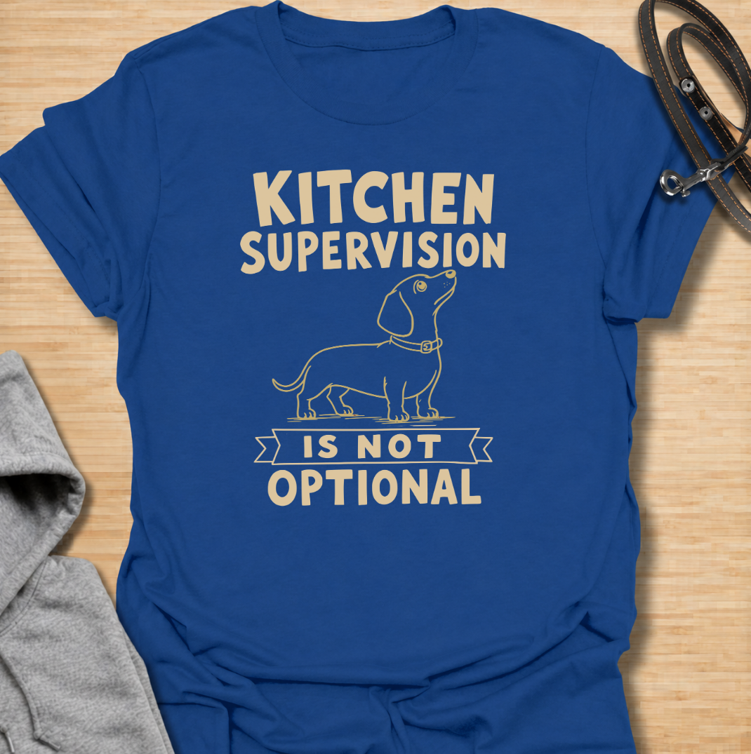 A funny dachshund T-shirt for anyone who never enters the kitchen without their four-legged supervisor close behind. Featuring a clean vintage-inspired dachshund illustration and the phrase “Kitchen Supervision Is Not Optional,” this design captures one of the breed’s most familiar habits. Perfect for dachshund moms, dachshund dads, sausage dog owners, and anyone whose dog appears the moment food is involved. A playful everyday tee for fans of dachshund humor, wiener dogs, and food-obsessed pups.