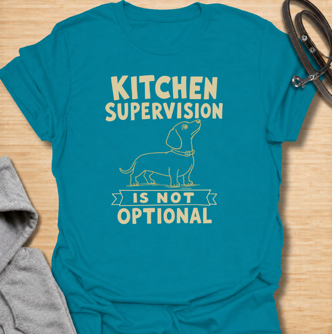 A funny dachshund T-shirt for anyone who never enters the kitchen without their four-legged supervisor close behind. Featuring a clean vintage-inspired dachshund illustration and the phrase “Kitchen Supervision Is Not Optional,” this design captures one of the breed’s most familiar habits. Perfect for dachshund moms, dachshund dads, sausage dog owners, and anyone whose dog appears the moment food is involved. A playful everyday tee for fans of dachshund humor, wiener dogs, and food-obsessed pups.