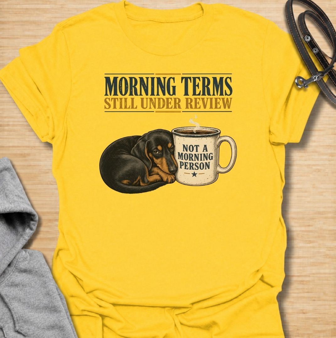 A funny dachshund T-shirt for anyone whose mornings require coffee, patience, and very limited conversation. Featuring a sleepy dachshund curled beside a coffee mug with the phrases “Morning Terms Still Under Review” and “Not a Morning Person,” this design has a dry, relatable sense of humor. Perfect for dachshund moms, dachshund dads, coffee lovers, and anyone who prefers a slow start to the day. A fun everyday tee combining dachshund humor, coffee culture, and an unmistakably grumpy morning mood.