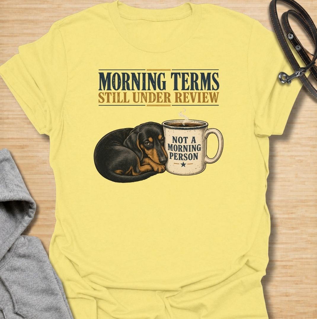 A funny dachshund T-shirt for anyone whose mornings require coffee, patience, and very limited conversation. Featuring a sleepy dachshund curled beside a coffee mug with the phrases “Morning Terms Still Under Review” and “Not a Morning Person,” this design has a dry, relatable sense of humor. Perfect for dachshund moms, dachshund dads, coffee lovers, and anyone who prefers a slow start to the day. A fun everyday tee combining dachshund humor, coffee culture, and an unmistakably grumpy morning mood.