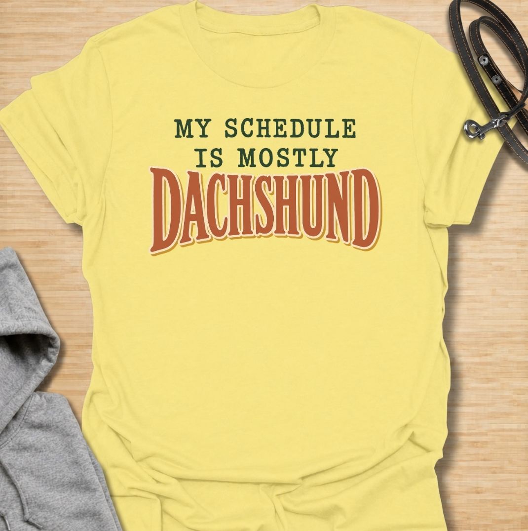 A funny dachshund T-shirt for anyone whose daily plans somehow revolve around their favorite little dog. Featuring the phrase “My Schedule Is Mostly Dachshund” in bold vintage-inspired typography, this design is simple, punchy, and easy to wear. Perfect for dachshund moms, dachshund dads, sausage dog owners, and anyone whose calendar is permanently shaped around walks, cuddles, and dachshund demands. A fun everyday tee for dog lovers who know exactly who really controls the schedule.
