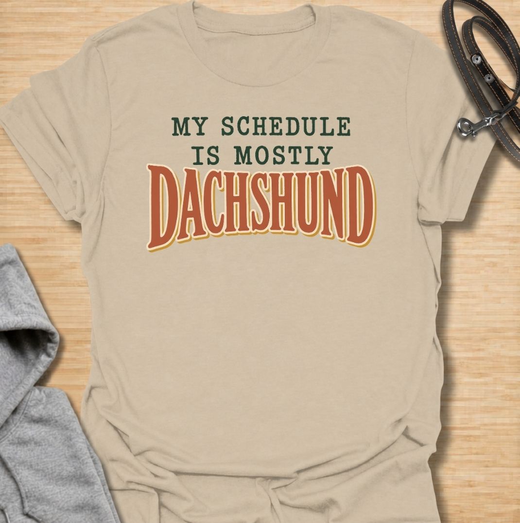 A funny dachshund T-shirt for anyone whose daily plans somehow revolve around their favorite little dog. Featuring the phrase “My Schedule Is Mostly Dachshund” in bold vintage-inspired typography, this design is simple, punchy, and easy to wear. Perfect for dachshund moms, dachshund dads, sausage dog owners, and anyone whose calendar is permanently shaped around walks, cuddles, and dachshund demands. A fun everyday tee for dog lovers who know exactly who really controls the schedule.