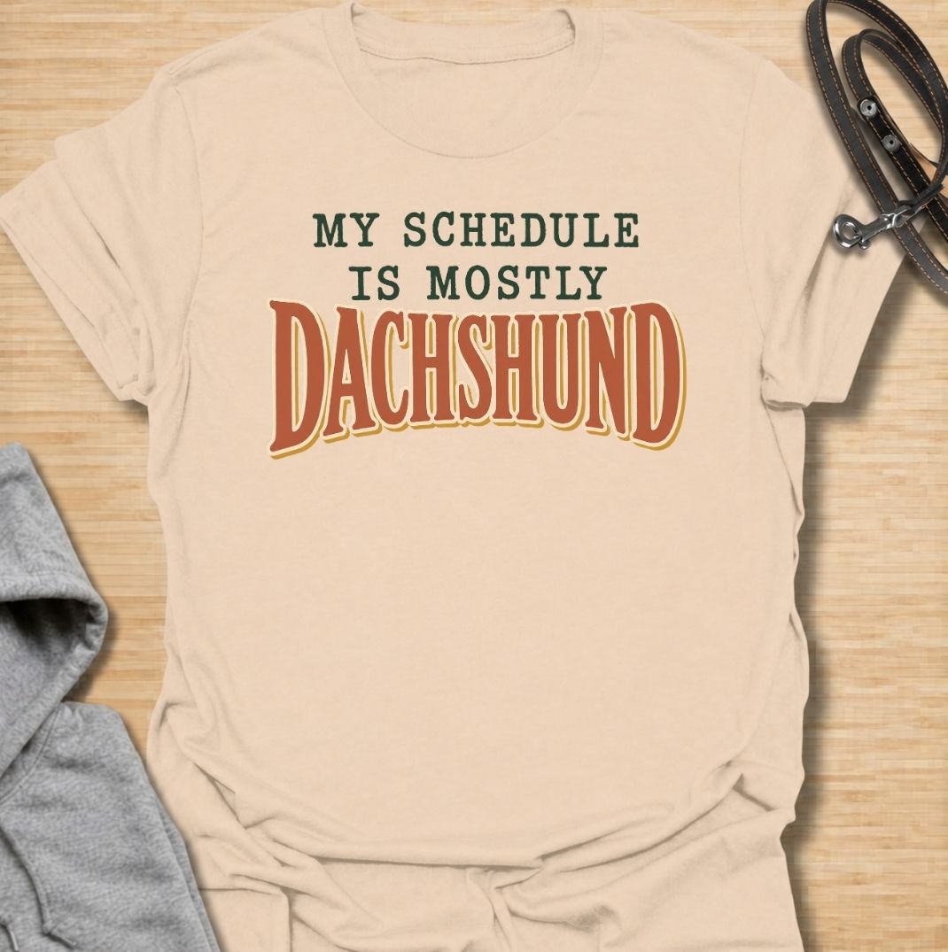A funny dachshund T-shirt for anyone whose daily plans somehow revolve around their favorite little dog. Featuring the phrase “My Schedule Is Mostly Dachshund” in bold vintage-inspired typography, this design is simple, punchy, and easy to wear. Perfect for dachshund moms, dachshund dads, sausage dog owners, and anyone whose calendar is permanently shaped around walks, cuddles, and dachshund demands. A fun everyday tee for dog lovers who know exactly who really controls the schedule.