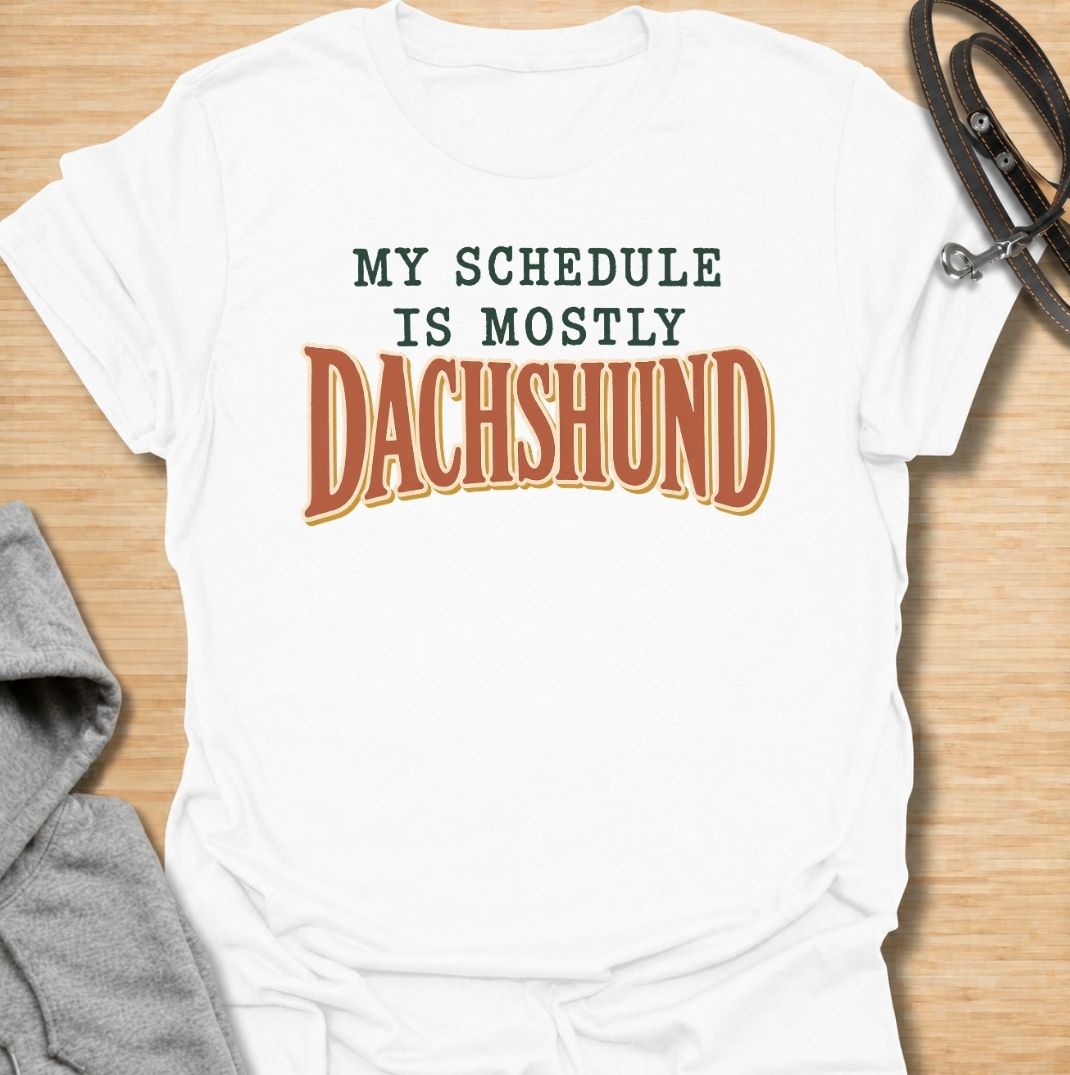 A funny dachshund T-shirt for anyone whose daily plans somehow revolve around their favorite little dog. Featuring the phrase “My Schedule Is Mostly Dachshund” in bold vintage-inspired typography, this design is simple, punchy, and easy to wear. Perfect for dachshund moms, dachshund dads, sausage dog owners, and anyone whose calendar is permanently shaped around walks, cuddles, and dachshund demands. A fun everyday tee for dog lovers who know exactly who really controls the schedule.