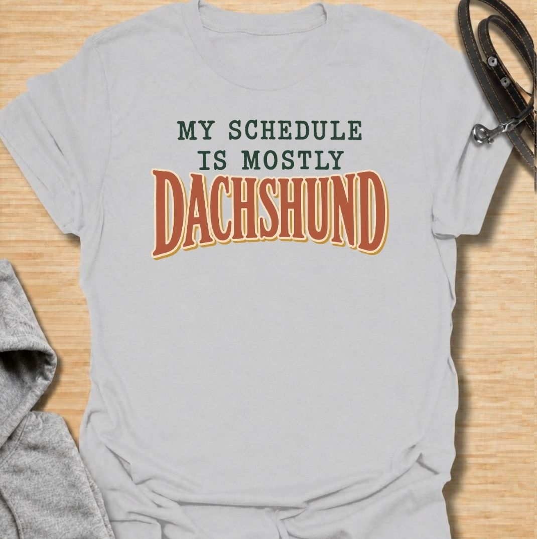 A funny dachshund T-shirt for anyone whose daily plans somehow revolve around their favorite little dog. Featuring the phrase “My Schedule Is Mostly Dachshund” in bold vintage-inspired typography, this design is simple, punchy, and easy to wear. Perfect for dachshund moms, dachshund dads, sausage dog owners, and anyone whose calendar is permanently shaped around walks, cuddles, and dachshund demands. A fun everyday tee for dog lovers who know exactly who really controls the schedule.