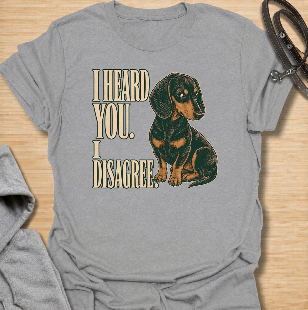 A funny dachshund T-shirt for anyone who knows that hearing a command and agreeing with it are two completely different things. Featuring the phrase “I Heard You. I Disagree.” with a vintage-style dachshund giving the perfect skeptical side-eye, this design captures the breed’s famously stubborn personality. Ideal for dachshund moms, dachshund dads, sausage dog owners, and anyone familiar with selective listening from a determined little dog. A playful everyday tee for fans of dachshund humor, wiener dog at