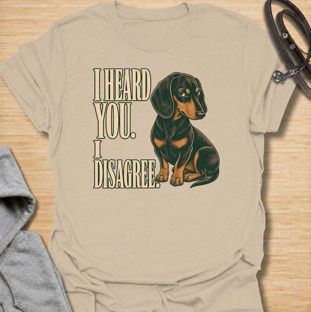 A funny dachshund T-shirt for anyone who knows that hearing a command and agreeing with it are two completely different things. Featuring the phrase “I Heard You. I Disagree.” with a vintage-style dachshund giving the perfect skeptical side-eye, this design captures the breed’s famously stubborn personality. Ideal for dachshund moms, dachshund dads, sausage dog owners, and anyone familiar with selective listening from a determined little dog. A playful everyday tee for fans of dachshund humor, wiener dog at