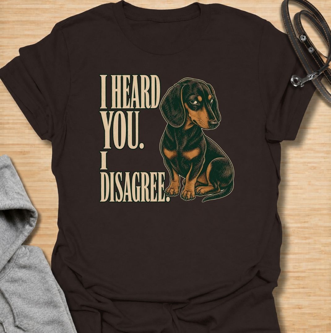 A funny dachshund T-shirt for anyone who knows that hearing a command and agreeing with it are two completely different things. Featuring the phrase “I Heard You. I Disagree.” with a vintage-style dachshund giving the perfect skeptical side-eye, this design captures the breed’s famously stubborn personality. Ideal for dachshund moms, dachshund dads, sausage dog owners, and anyone familiar with selective listening from a determined little dog. A playful everyday tee for fans of dachshund humor, wiener dog at