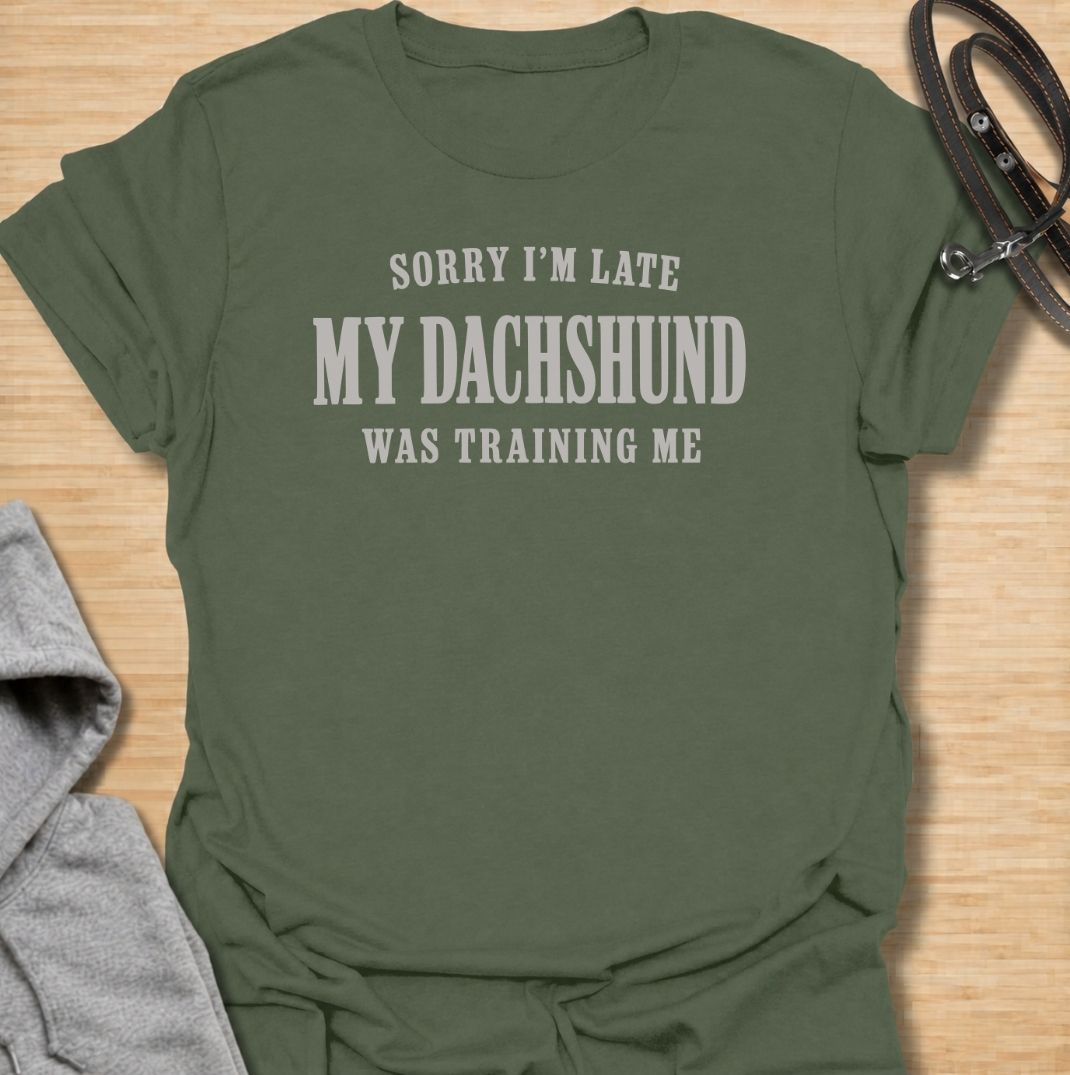 A funny dachshund T-shirt for anyone who knows the dog is usually the one in charge. Featuring the phrase “Sorry I’m Late, My Dachshund Was Training Me,” this clean text-based design plays on the breed’s stubborn, clever personality. Perfect for dachshund moms, dachshund dads, sausage dog owners, and anyone whose plans regularly revolve around their dog. A simple everyday tee for fans of dachshund humor, funny dog sayings, and breed-specific gifts.