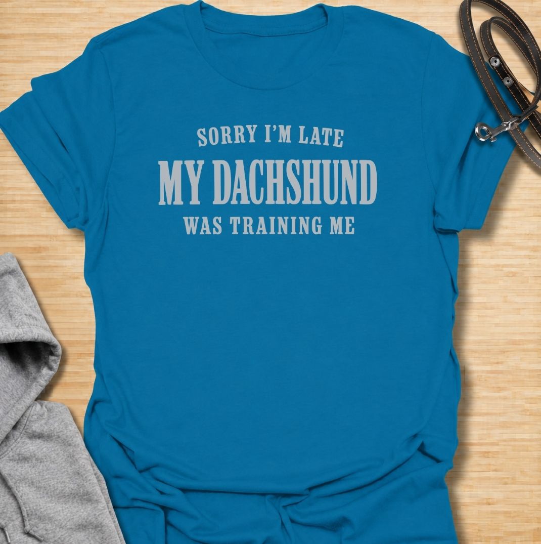 A funny dachshund T-shirt for anyone who knows the dog is usually the one in charge. Featuring the phrase “Sorry I’m Late, My Dachshund Was Training Me,” this clean text-based design plays on the breed’s stubborn, clever personality. Perfect for dachshund moms, dachshund dads, sausage dog owners, and anyone whose plans regularly revolve around their dog. A simple everyday tee for fans of dachshund humor, funny dog sayings, and breed-specific gifts.