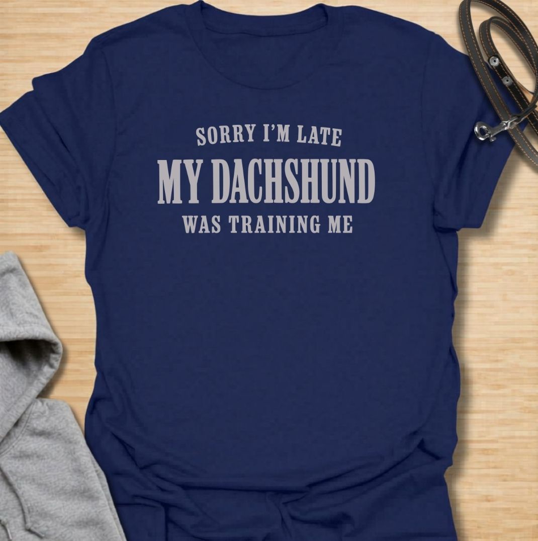 A funny dachshund T-shirt for anyone who knows the dog is usually the one in charge. Featuring the phrase “Sorry I’m Late, My Dachshund Was Training Me,” this clean text-based design plays on the breed’s stubborn, clever personality. Perfect for dachshund moms, dachshund dads, sausage dog owners, and anyone whose plans regularly revolve around their dog. A simple everyday tee for fans of dachshund humor, funny dog sayings, and breed-specific gifts.