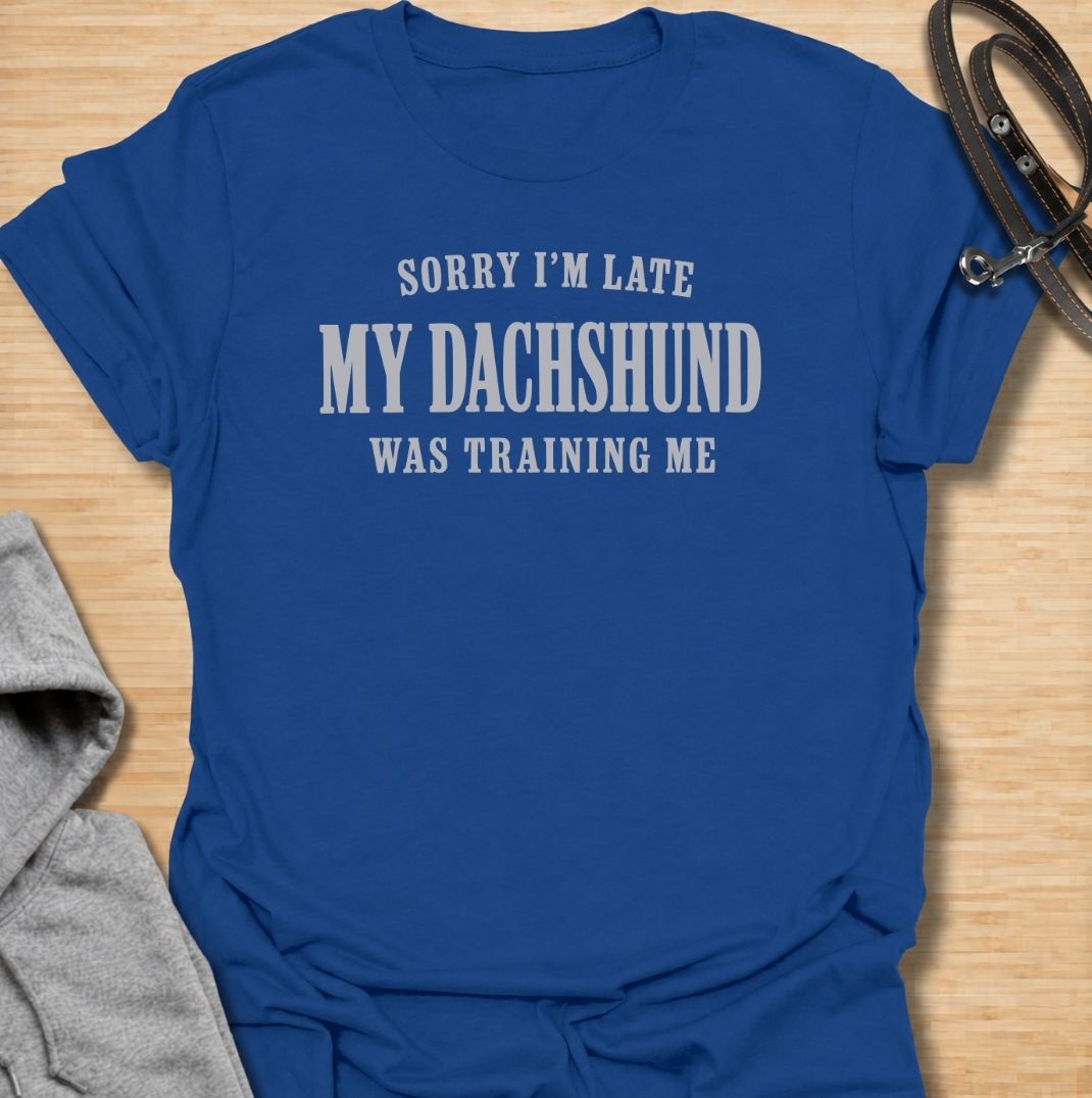 A funny dachshund T-shirt for anyone who knows the dog is usually the one in charge. Featuring the phrase “Sorry I’m Late, My Dachshund Was Training Me,” this clean text-based design plays on the breed’s stubborn, clever personality. Perfect for dachshund moms, dachshund dads, sausage dog owners, and anyone whose plans regularly revolve around their dog. A simple everyday tee for fans of dachshund humor, funny dog sayings, and breed-specific gifts.