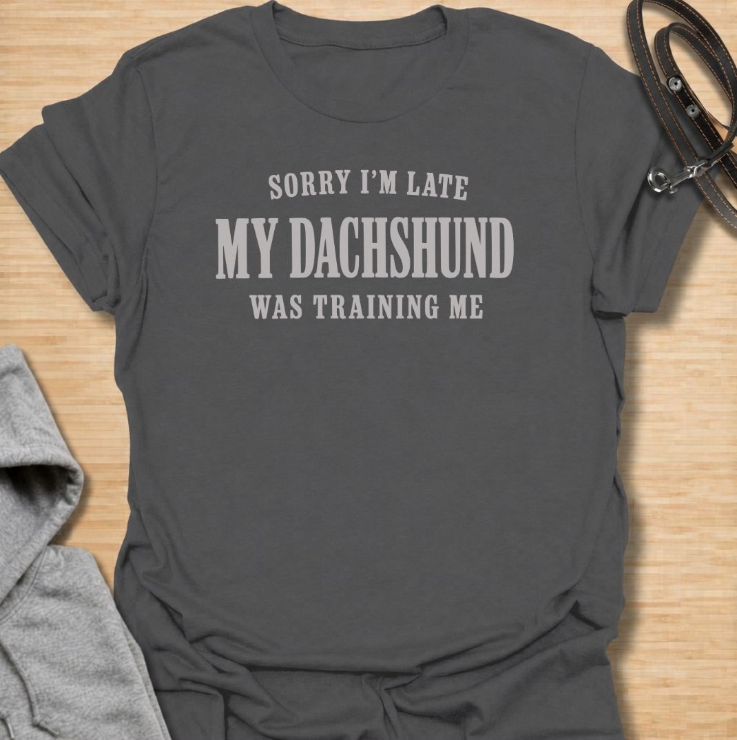 A funny dachshund T-shirt for anyone who knows the dog is usually the one in charge. Featuring the phrase “Sorry I’m Late, My Dachshund Was Training Me,” this clean text-based design plays on the breed’s stubborn, clever personality. Perfect for dachshund moms, dachshund dads, sausage dog owners, and anyone whose plans regularly revolve around their dog. A simple everyday tee for fans of dachshund humor, funny dog sayings, and breed-specific gifts.