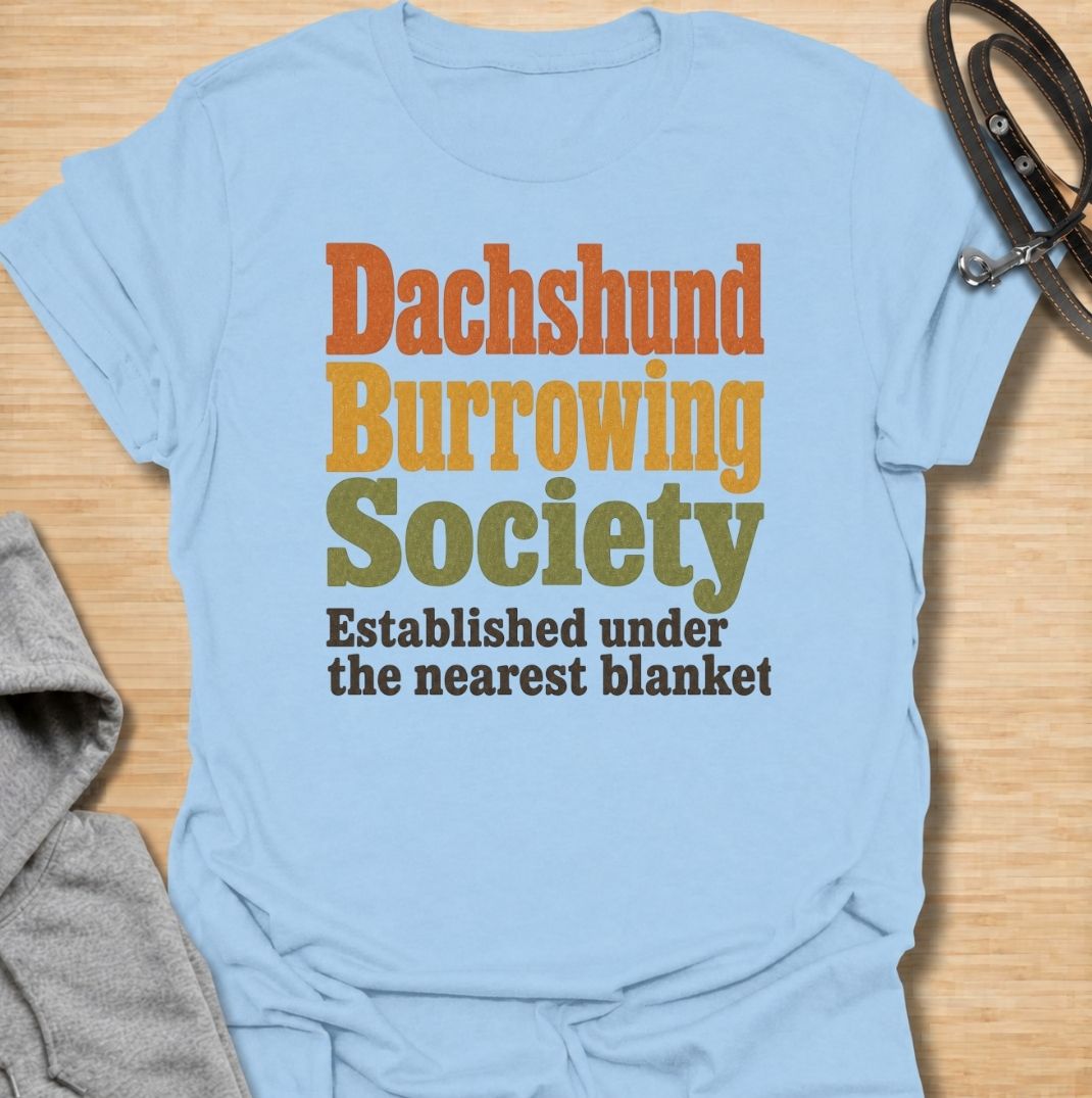 A funny dachshund T-shirt for anyone who knows the fastest way to find a sausage dog is to check under the nearest blanket. Featuring the phrase “Dachshund Burrowing Society — Established Under the Nearest Blanket,” this retro text design celebrates one of the breed’s most familiar habits. Perfect for dachshund moms, dachshund dads, doxie owners, and anyone whose dog treats blankets like a second home. A cozy, humorous everyday tee for fans of dachshund personality, burrowing behavior, and breed-specific do