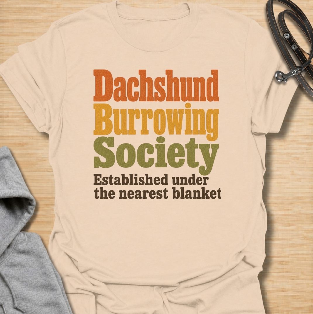 A funny dachshund T-shirt for anyone who knows the fastest way to find a sausage dog is to check under the nearest blanket. Featuring the phrase “Dachshund Burrowing Society — Established Under the Nearest Blanket,” this retro text design celebrates one of the breed’s most familiar habits. Perfect for dachshund moms, dachshund dads, doxie owners, and anyone whose dog treats blankets like a second home. A cozy, humorous everyday tee for fans of dachshund personality, burrowing behavior, and breed-specific do