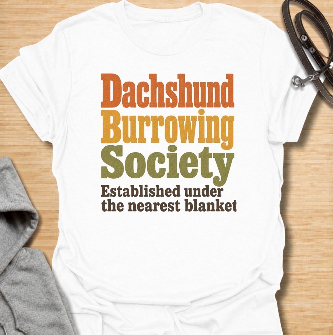 A funny dachshund T-shirt for anyone who knows the fastest way to find a sausage dog is to check under the nearest blanket. Featuring the phrase “Dachshund Burrowing Society — Established Under the Nearest Blanket,” this retro text design celebrates one of the breed’s most familiar habits. Perfect for dachshund moms, dachshund dads, doxie owners, and anyone whose dog treats blankets like a second home. A cozy, humorous everyday tee for fans of dachshund personality, burrowing behavior, and breed-specific do