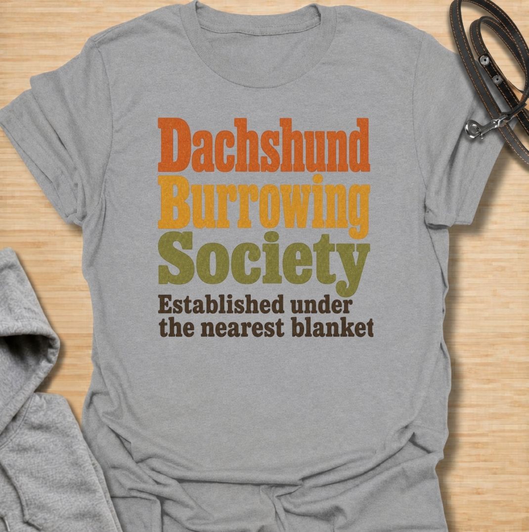 A funny dachshund T-shirt for anyone who knows the fastest way to find a sausage dog is to check under the nearest blanket. Featuring the phrase “Dachshund Burrowing Society — Established Under the Nearest Blanket,” this retro text design celebrates one of the breed’s most familiar habits. Perfect for dachshund moms, dachshund dads, doxie owners, and anyone whose dog treats blankets like a second home. A cozy, humorous everyday tee for fans of dachshund personality, burrowing behavior, and breed-specific do