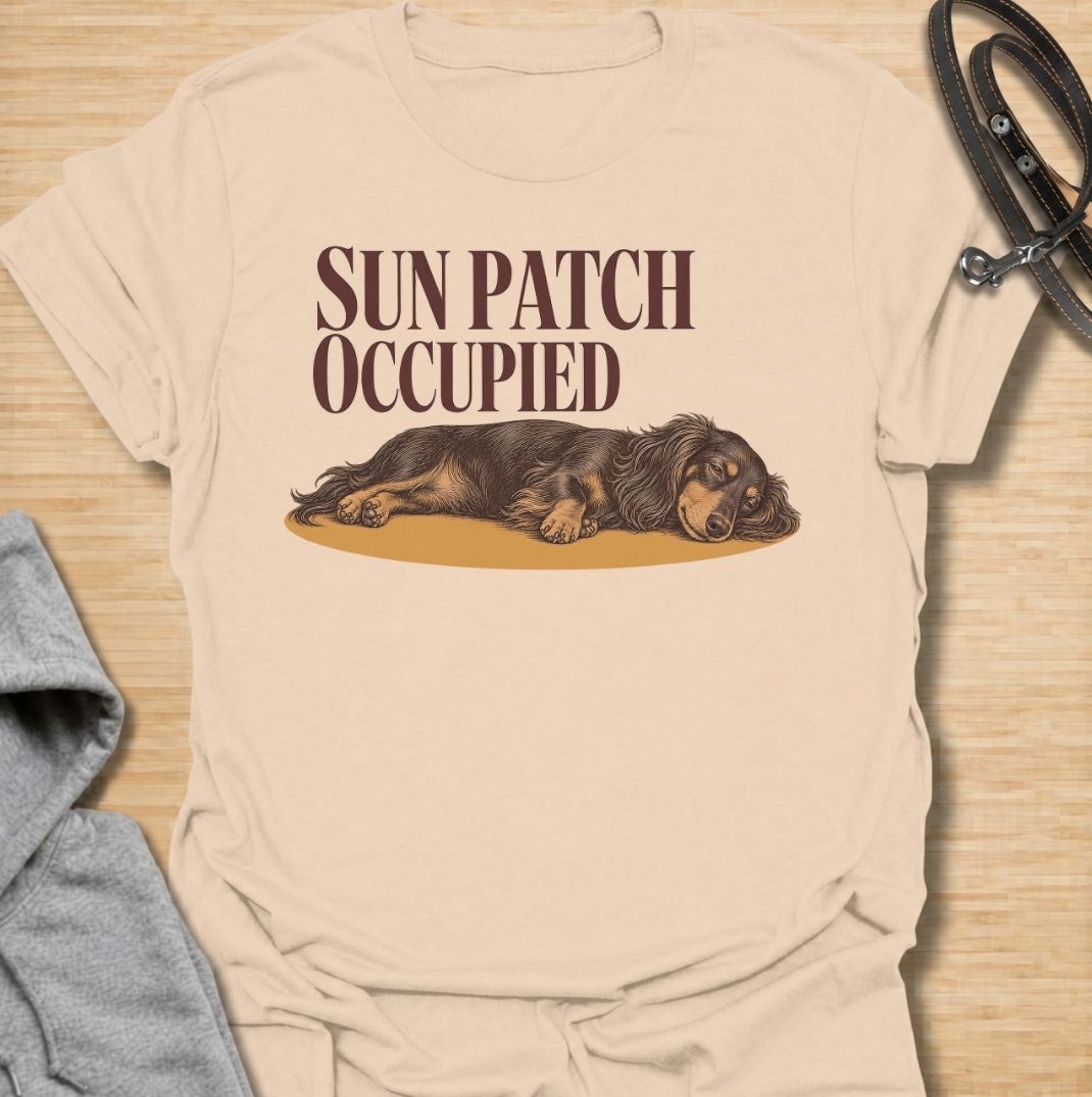 A funny dachshund T-shirt for anyone who knows the best sunny spot in the house is already taken. Featuring the phrase “Sun Patch Occupied” with a relaxed dachshund stretched out in the warmth, this design captures one of the breed’s most familiar little habits. Perfect for dachshund moms, dachshund dads, sausage dog owners, and anyone whose dog follows every patch of sunshine around the room. A cozy everyday tee for fans of dachshund humor, sleepy dogs, and breed-specific gifts.