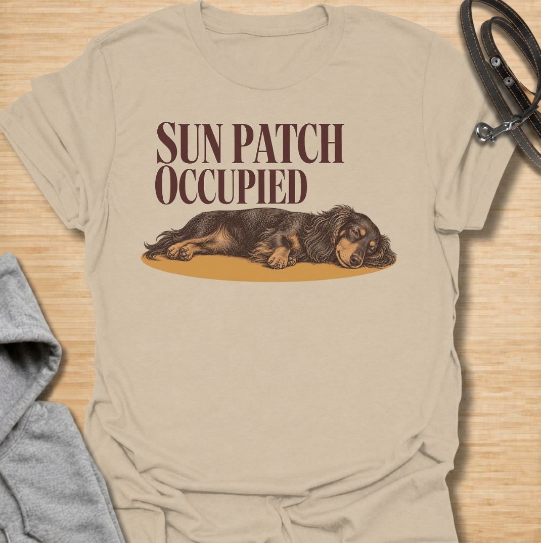 A funny dachshund T-shirt for anyone who knows the best sunny spot in the house is already taken. Featuring the phrase “Sun Patch Occupied” with a relaxed dachshund stretched out in the warmth, this design captures one of the breed’s most familiar little habits. Perfect for dachshund moms, dachshund dads, sausage dog owners, and anyone whose dog follows every patch of sunshine around the room. A cozy everyday tee for fans of dachshund humor, sleepy dogs, and breed-specific gifts.