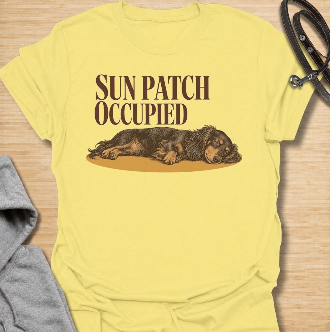 A funny dachshund T-shirt for anyone who knows the best sunny spot in the house is already taken. Featuring the phrase “Sun Patch Occupied” with a relaxed dachshund stretched out in the warmth, this design captures one of the breed’s most familiar little habits. Perfect for dachshund moms, dachshund dads, sausage dog owners, and anyone whose dog follows every patch of sunshine around the room. A cozy everyday tee for fans of dachshund humor, sleepy dogs, and breed-specific gifts.