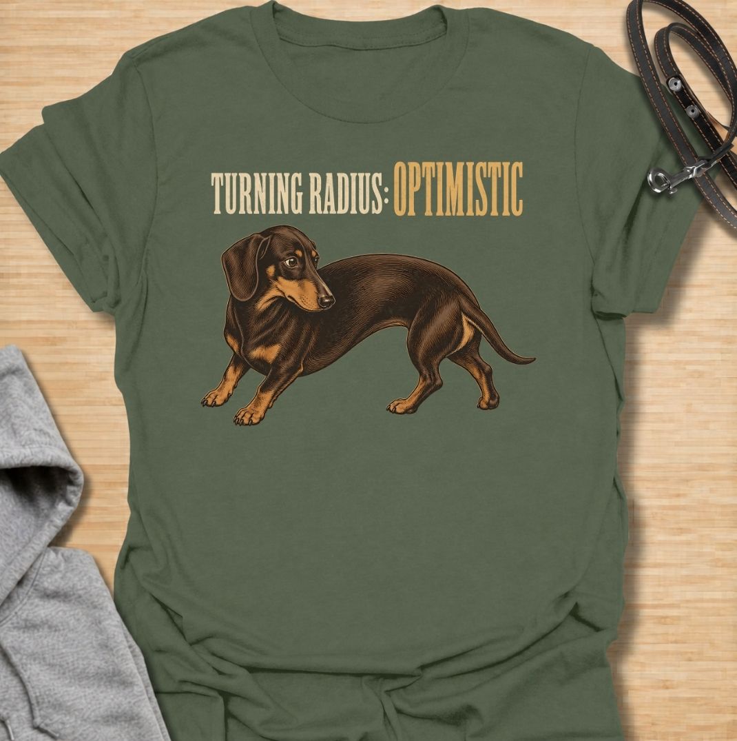 A funny dachshund T-shirt for anyone who knows these long little dogs are not exactly built for tight corners. Featuring the phrase “Turning Radius: Optimistic” with a curved dachshund illustration, this design turns the breed’s famously elongated shape into a clever inside joke. Perfect for dachshund moms, dachshund dads, sausage dog owners, and anyone who loves dry breed-specific humor. A playful everyday tee for fans of wiener dogs, doxies, and small dogs with slightly questionable maneuverability.