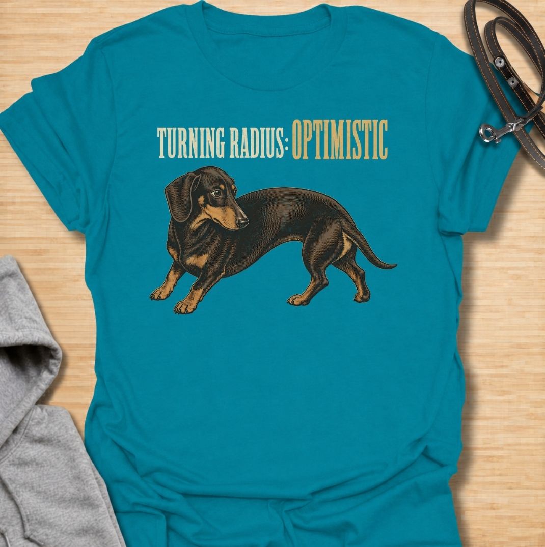 A funny dachshund T-shirt for anyone who knows these long little dogs are not exactly built for tight corners. Featuring the phrase “Turning Radius: Optimistic” with a curved dachshund illustration, this design turns the breed’s famously elongated shape into a clever inside joke. Perfect for dachshund moms, dachshund dads, sausage dog owners, and anyone who loves dry breed-specific humor. A playful everyday tee for fans of wiener dogs, doxies, and small dogs with slightly questionable maneuverability.