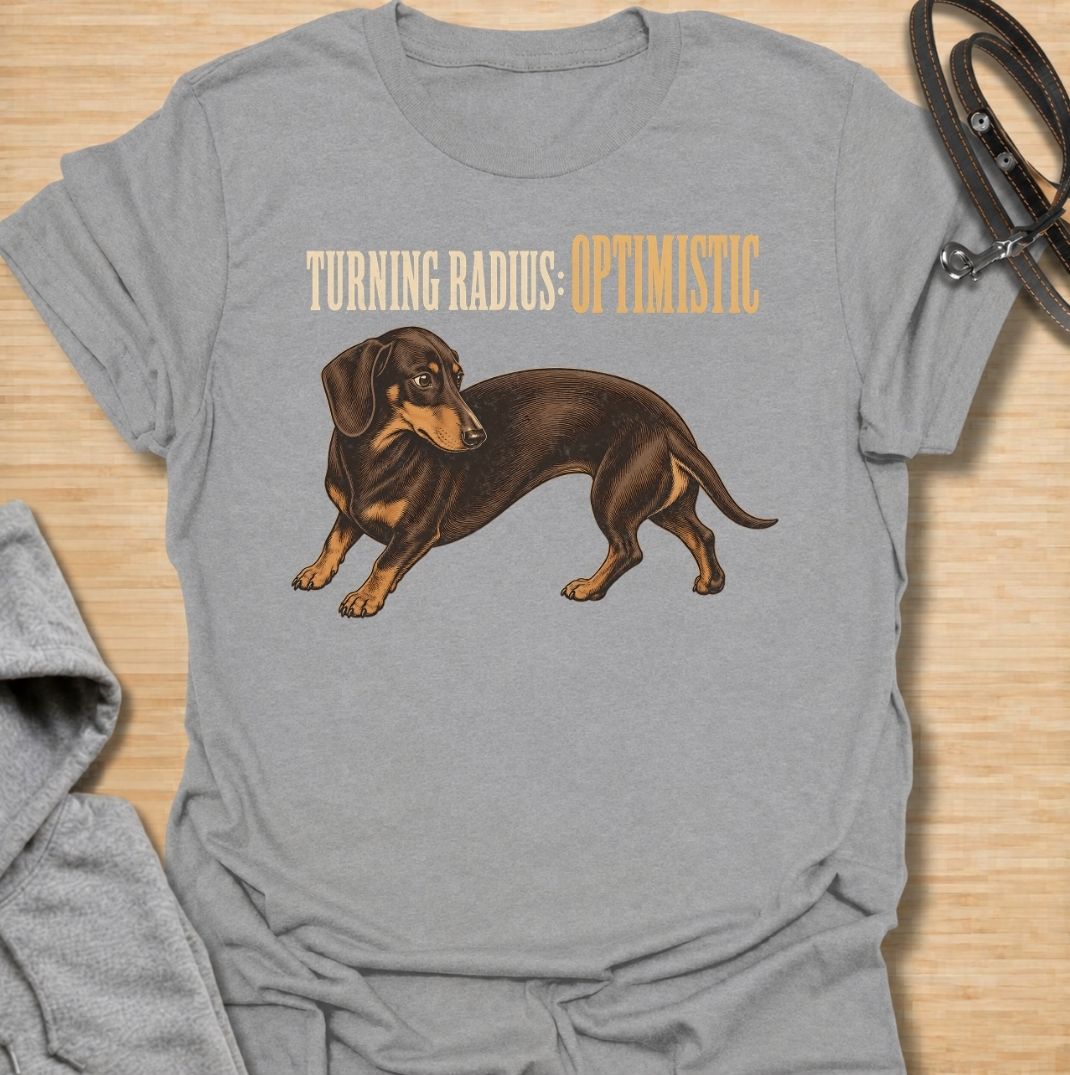 A funny dachshund T-shirt for anyone who knows these long little dogs are not exactly built for tight corners. Featuring the phrase “Turning Radius: Optimistic” with a curved dachshund illustration, this design turns the breed’s famously elongated shape into a clever inside joke. Perfect for dachshund moms, dachshund dads, sausage dog owners, and anyone who loves dry breed-specific humor. A playful everyday tee for fans of wiener dogs, doxies, and small dogs with slightly questionable maneuverability.