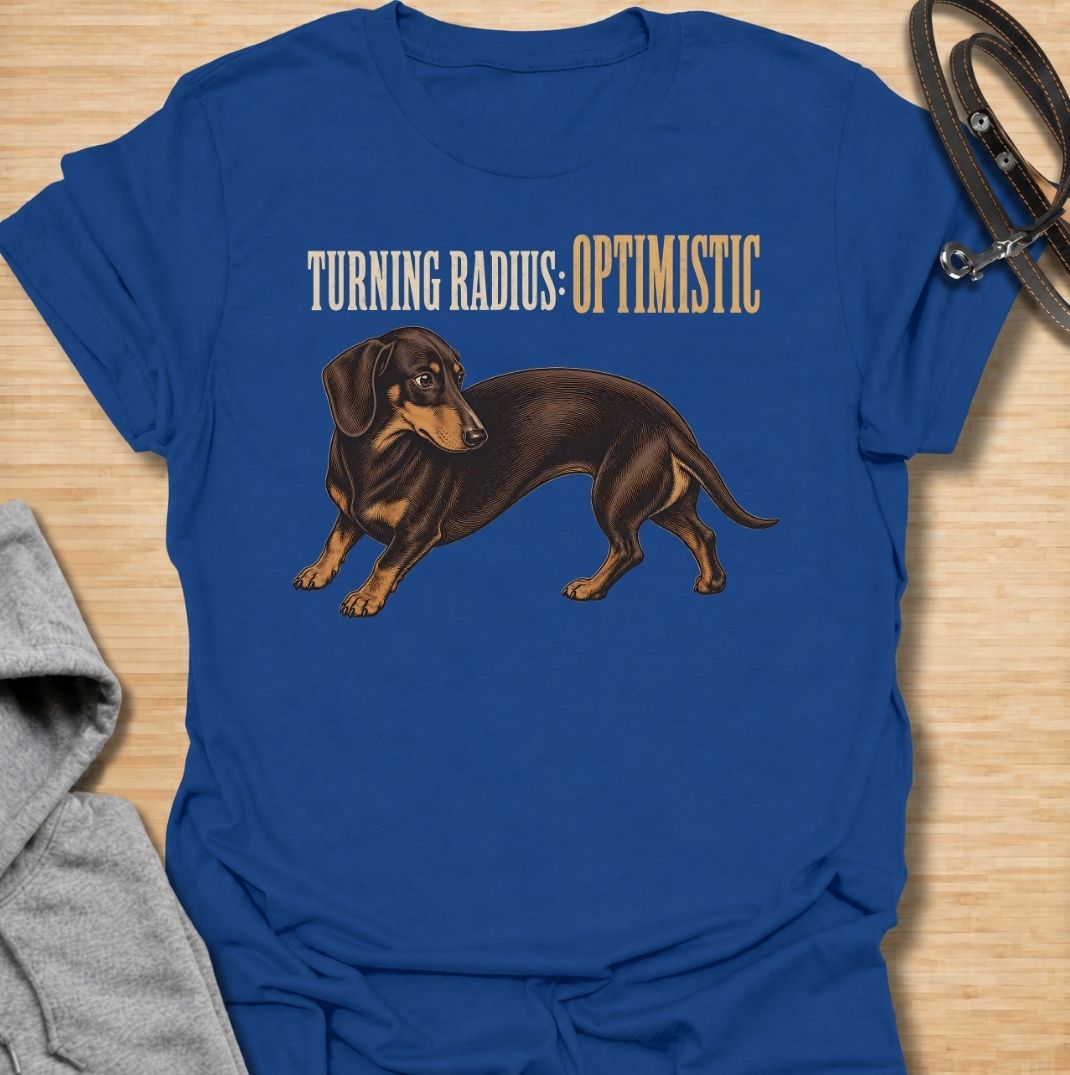 A funny dachshund T-shirt for anyone who knows these long little dogs are not exactly built for tight corners. Featuring the phrase “Turning Radius: Optimistic” with a curved dachshund illustration, this design turns the breed’s famously elongated shape into a clever inside joke. Perfect for dachshund moms, dachshund dads, sausage dog owners, and anyone who loves dry breed-specific humor. A playful everyday tee for fans of wiener dogs, doxies, and small dogs with slightly questionable maneuverability.