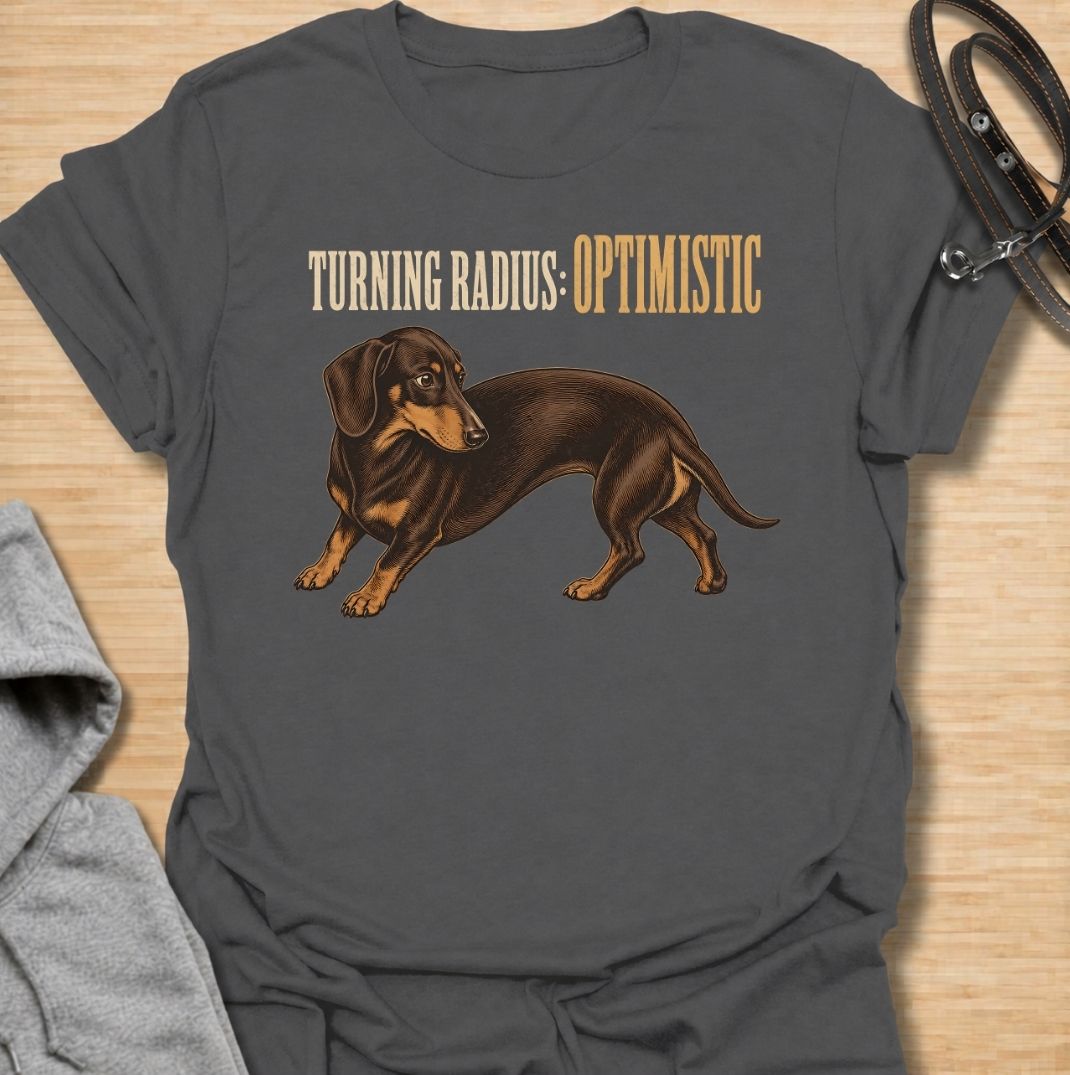 A funny dachshund T-shirt for anyone who knows these long little dogs are not exactly built for tight corners. Featuring the phrase “Turning Radius: Optimistic” with a curved dachshund illustration, this design turns the breed’s famously elongated shape into a clever inside joke. Perfect for dachshund moms, dachshund dads, sausage dog owners, and anyone who loves dry breed-specific humor. A playful everyday tee for fans of wiener dogs, doxies, and small dogs with slightly questionable maneuverability.
