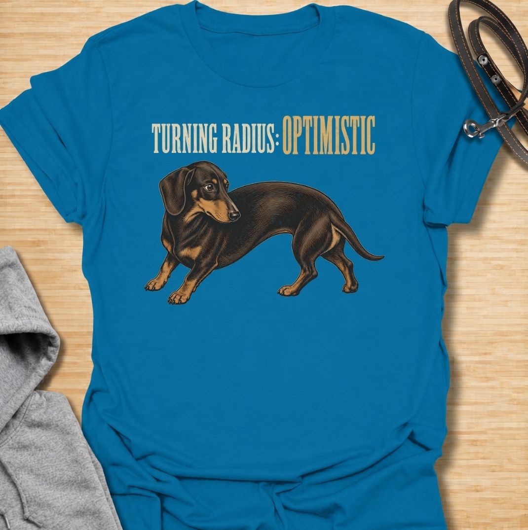 A funny dachshund T-shirt for anyone who knows these long little dogs are not exactly built for tight corners. Featuring the phrase “Turning Radius: Optimistic” with a curved dachshund illustration, this design turns the breed’s famously elongated shape into a clever inside joke. Perfect for dachshund moms, dachshund dads, sausage dog owners, and anyone who loves dry breed-specific humor. A playful everyday tee for fans of wiener dogs, doxies, and small dogs with slightly questionable maneuverability.