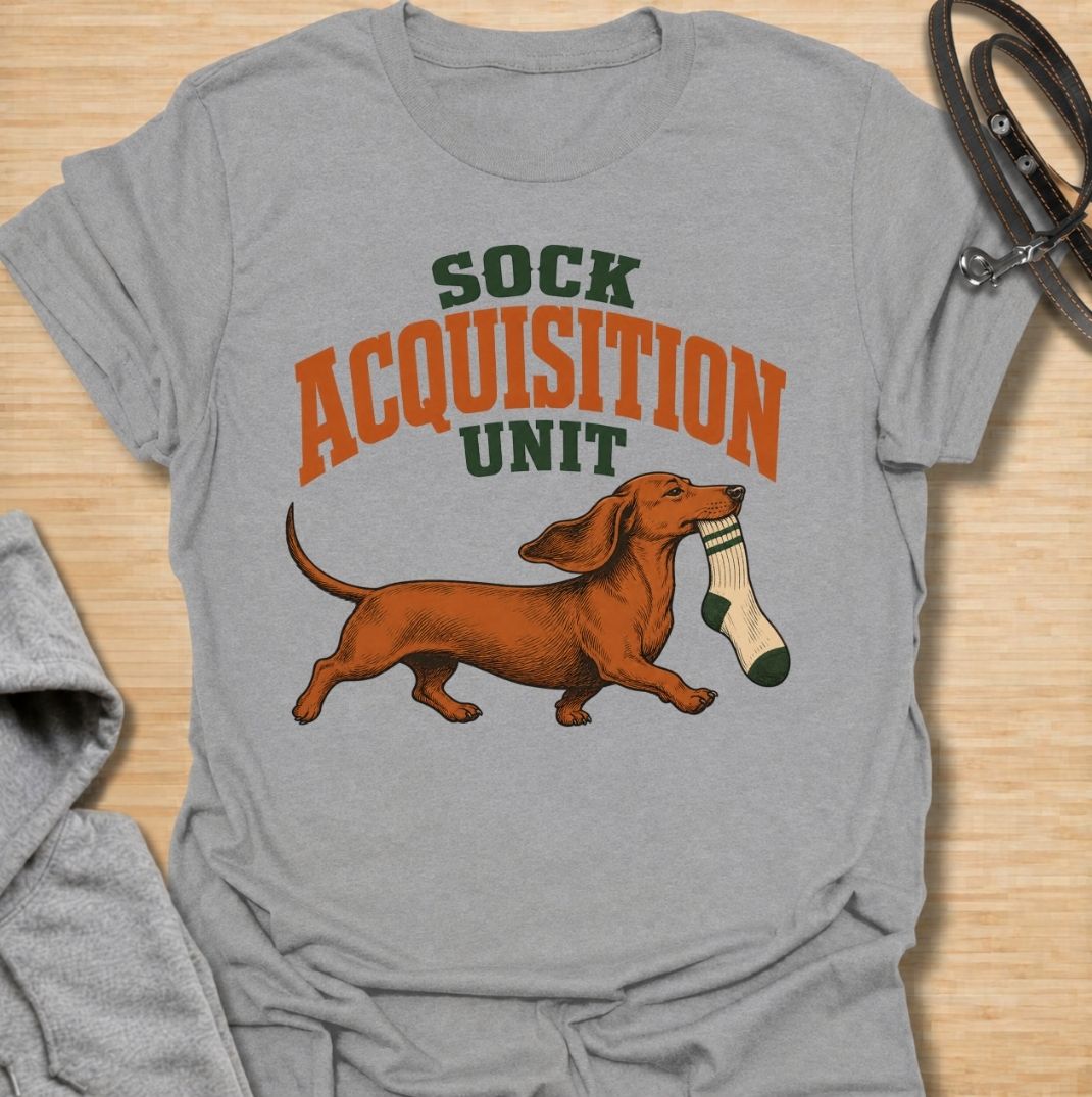 A funny dachshund T-shirt for anyone whose socks mysteriously disappear whenever their dog is nearby. Featuring the phrase “Sock Acquisition Unit” with a proud dachshund carrying its latest prize, this design captures one of those mischievous little habits dog owners know all too well. Perfect for dachshund moms, dachshund dads, sausage dog owners, and anyone living with a determined sock thief. A playful everyday tee for fans of dachshund humor, wiener dogs, and breed-specific dog gifts.