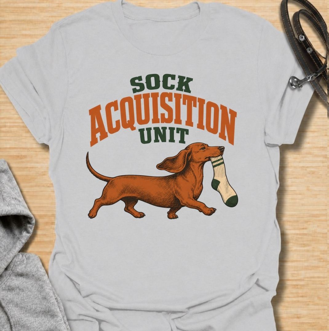 A funny dachshund T-shirt for anyone whose socks mysteriously disappear whenever their dog is nearby. Featuring the phrase “Sock Acquisition Unit” with a proud dachshund carrying its latest prize, this design captures one of those mischievous little habits dog owners know all too well. Perfect for dachshund moms, dachshund dads, sausage dog owners, and anyone living with a determined sock thief. A playful everyday tee for fans of dachshund humor, wiener dogs, and breed-specific dog gifts.