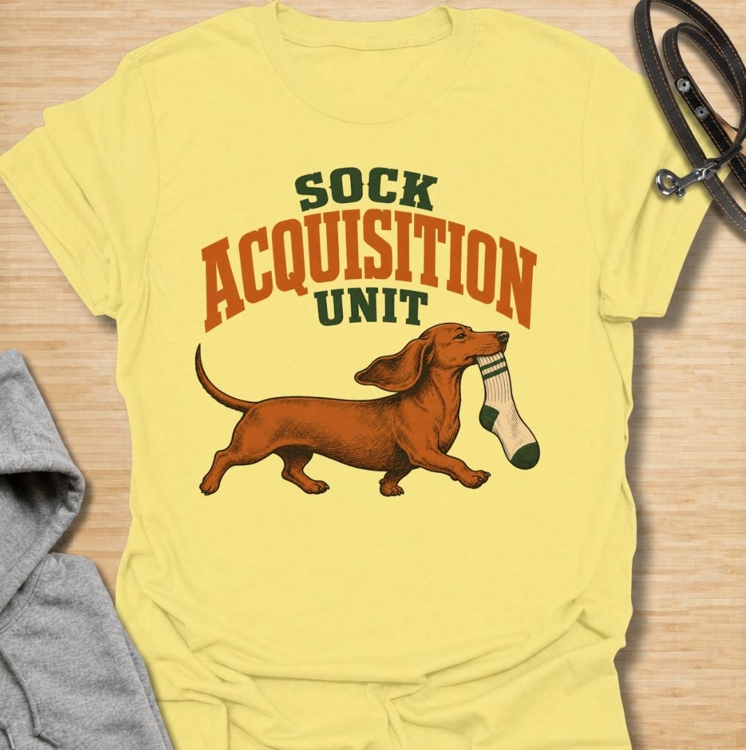 A funny dachshund T-shirt for anyone whose socks mysteriously disappear whenever their dog is nearby. Featuring the phrase “Sock Acquisition Unit” with a proud dachshund carrying its latest prize, this design captures one of those mischievous little habits dog owners know all too well. Perfect for dachshund moms, dachshund dads, sausage dog owners, and anyone living with a determined sock thief. A playful everyday tee for fans of dachshund humor, wiener dogs, and breed-specific dog gifts.